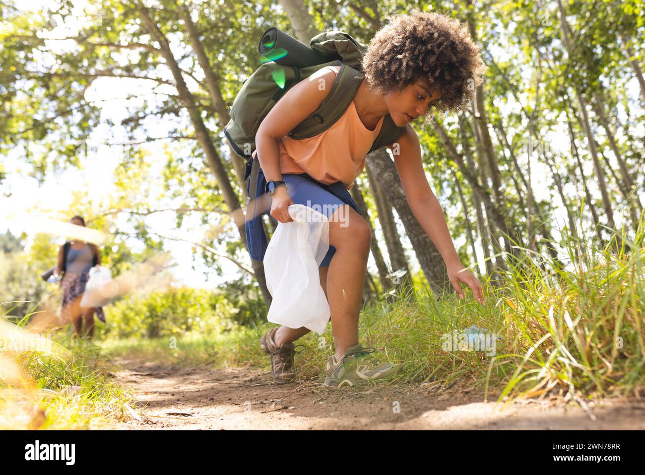 Una giovane donna birazziale raccoglie la spazzatura mentre fa trekking, promuovendo la tutela dell'ambiente Foto Stock