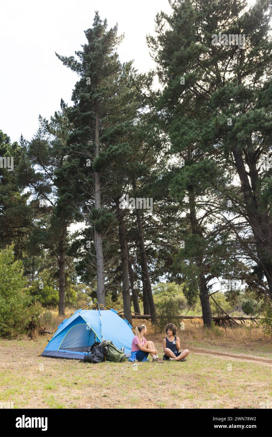 Due donne si rilassano accanto a una tenda blu in una tranquilla radura della foresta con spazio per le copie Foto Stock