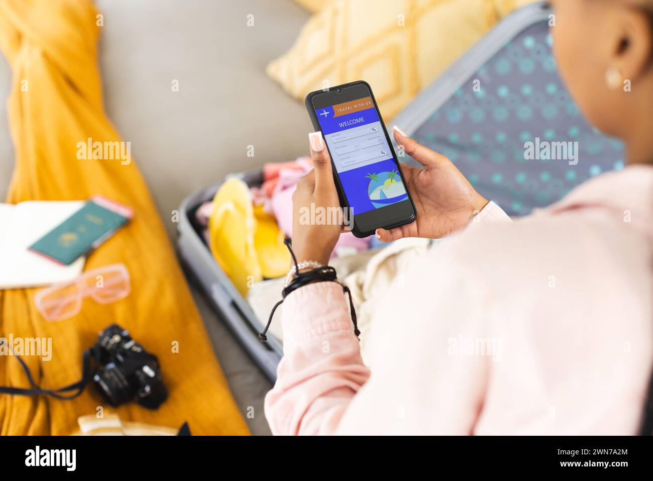 Una giovane donna afroamericana controlla il suo telefono, circondata da oggetti essenziali per il viaggio Foto Stock