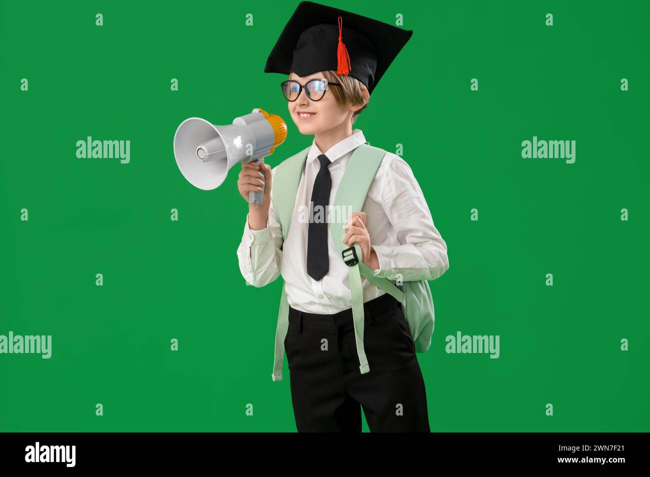 Bambino in cappello graduato con megafono su sfondo verde. Fine dell'anno scolastico Foto Stock