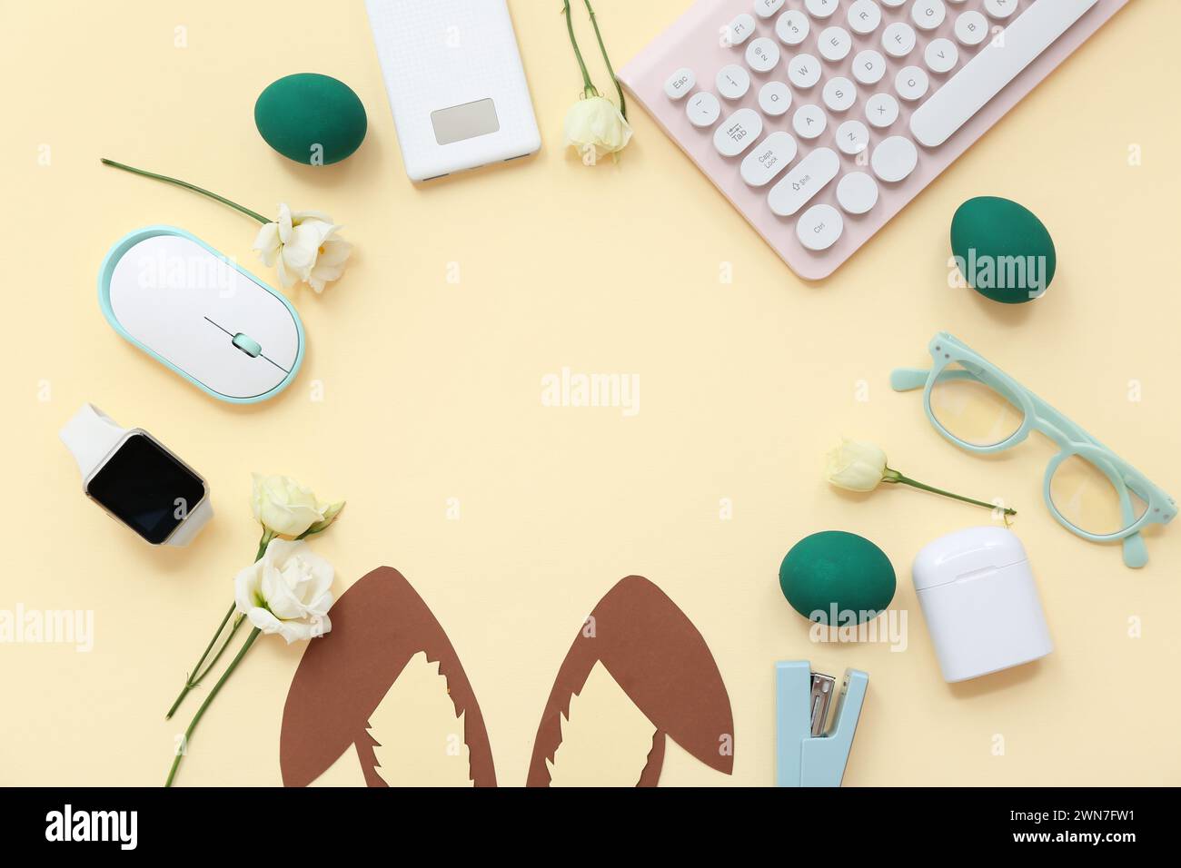 Cornice fatta di uova di Pasqua, carta, orecchie da coniglio, bicchieri, fiori, tastiera e mouse del computer su sfondo giallo Foto Stock