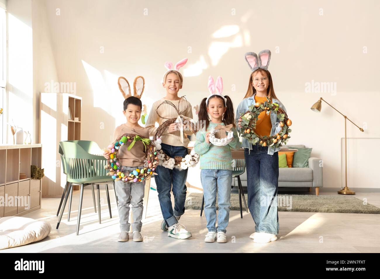 Bambini piccoli in orecchie da coniglio con ghirlande pasquali a casa Foto Stock