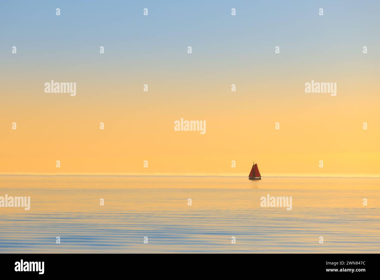 Uno yacht su un oceano calmo al tramonto con luce dorata. La nave si allontana tranquillamente su un mare vuoto godendosi una calda estate e la libertà. Un'immagine minimalista. Foto Stock