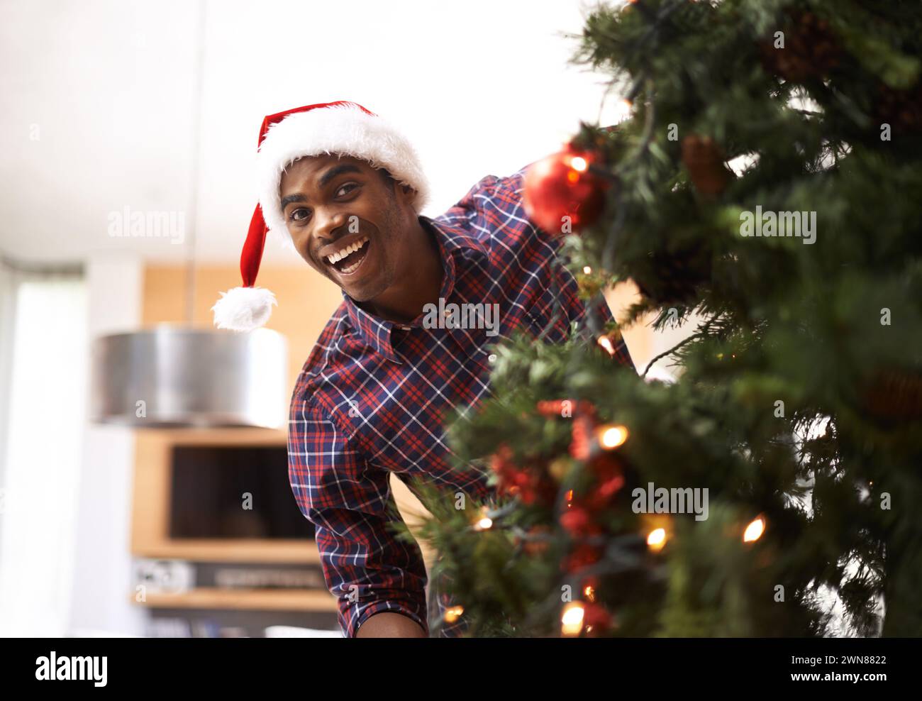 Ritratto, energia e uomo nero con albero di Natale nel soggiorno di casa per la decorazione o le vacanze. Sorridi, festeggiamenti a dicembre e felice giovane Foto Stock