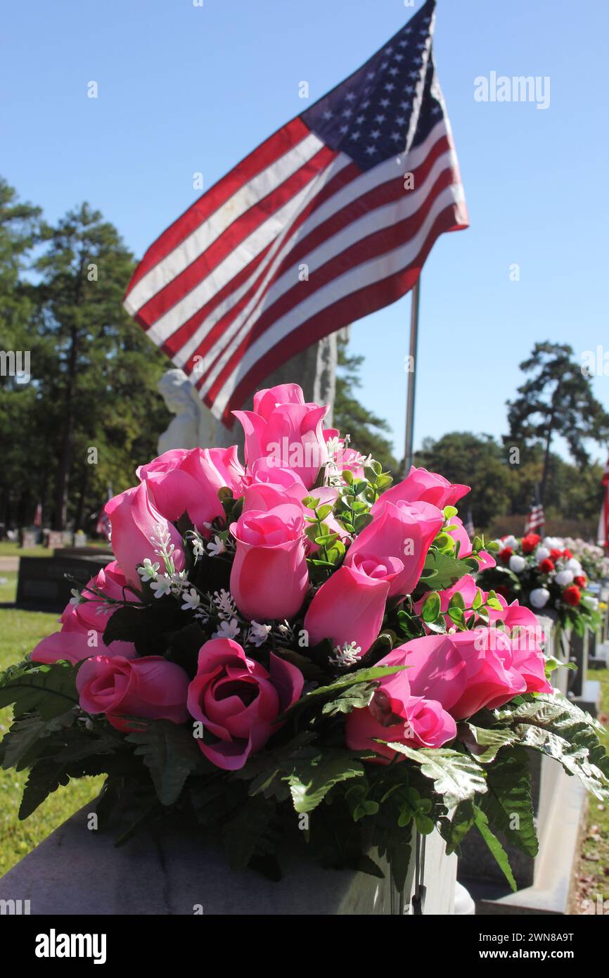 La bandiera degli Stati Uniti ondeggia dietro le rose sulle lapidi del cimitero Foto Stock