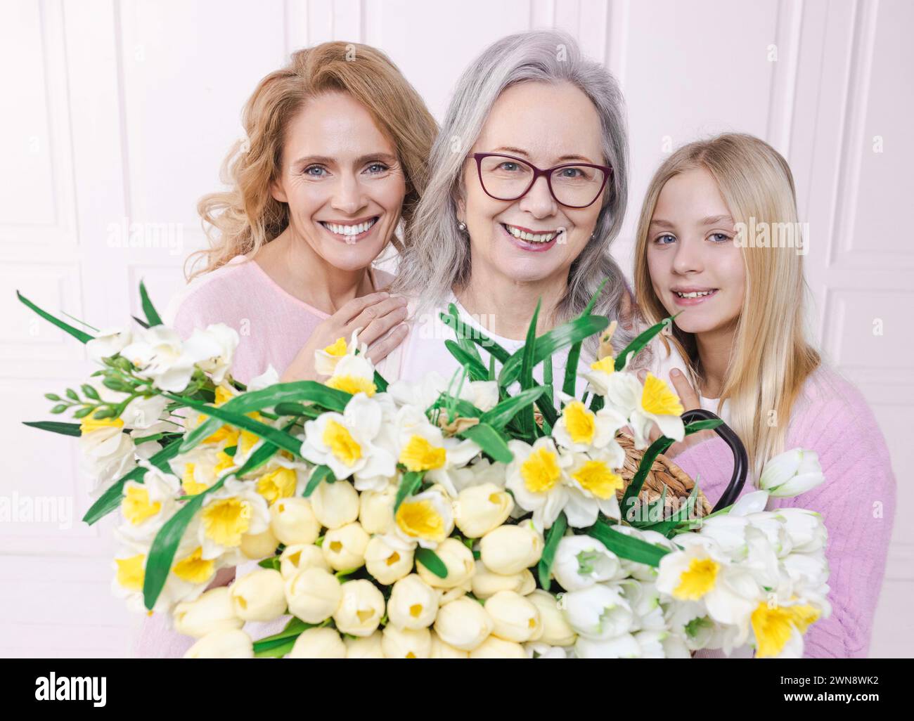 Belle donne di tre generazioni, durante l'incontro di famiglia. Madre, nonna e nipote abbracciano, sorridono e tengono in mano un grande bouquet di tulipani Foto Stock