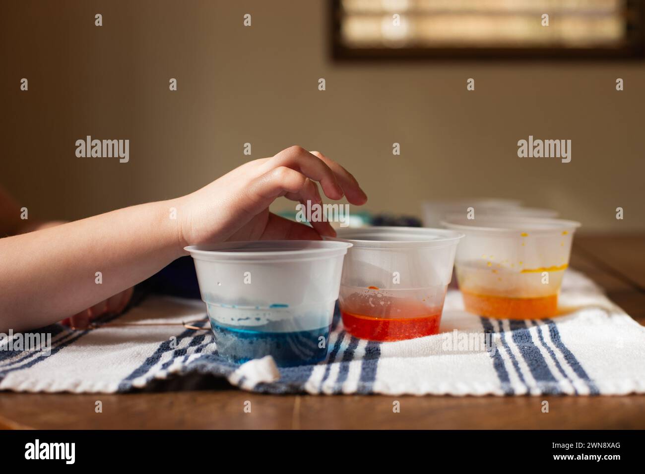 La mano del bambino raggiunge i bicchieri da colorare per cuocere le uova di pasqua Foto Stock