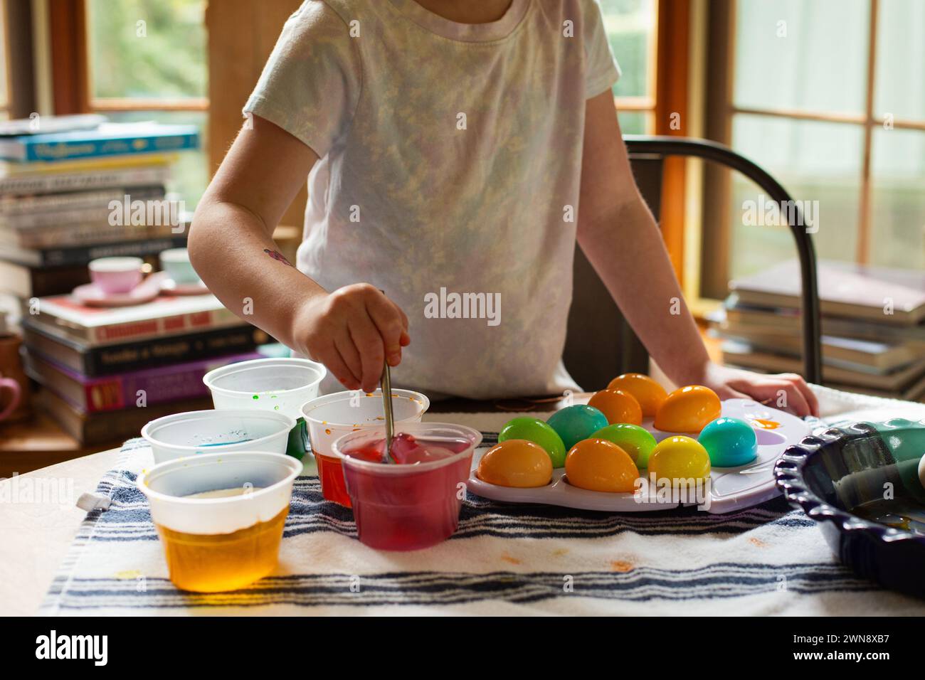 Bambina che mescola il colorante del cibo per le uova di Pasqua al tavolo della cucina Foto Stock