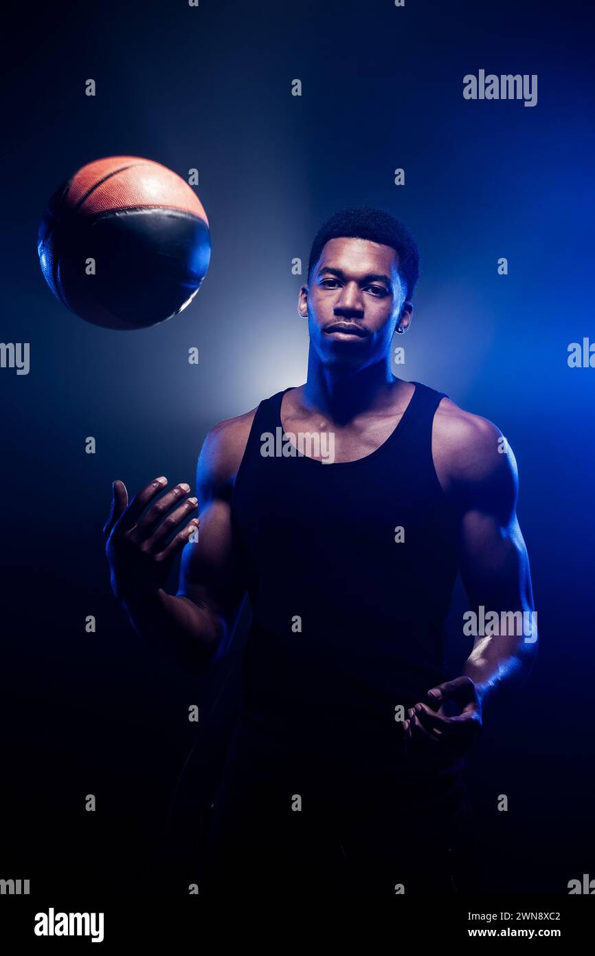 Giocatore di basket che lancia una palla contro lo sfondo blu nebbia. Uomo afroamericano che lancia palla da basket Foto Stock