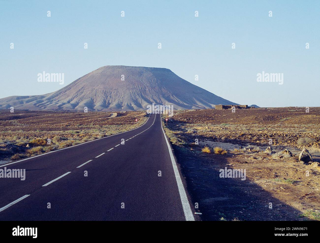 Strada solitaria e Vulcano. Isola di Fuerteventura, Isole Canarie, Spagna. Foto Stock