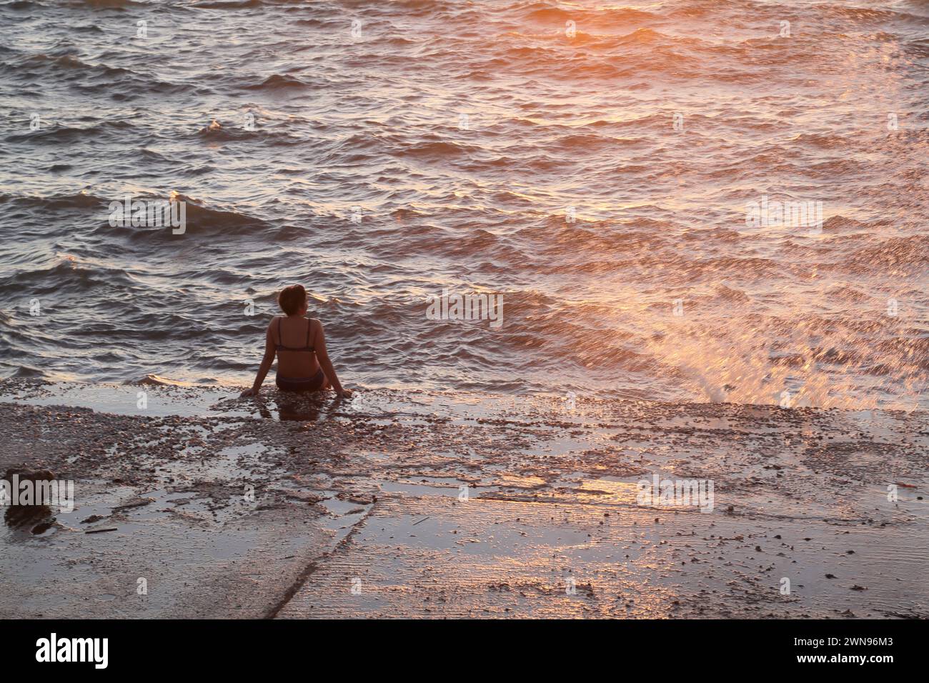 Turista seduto in mare con marea in arrivo che si schianta contro il muro Vouliagmeni Atene Grecia Foto Stock