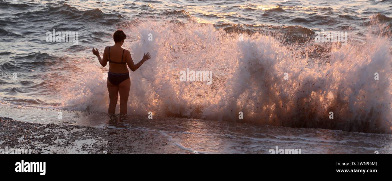 Turista in piedi in mare con marea che si schianta contro il muro Vouliagmeni Atene Grecia Foto Stock