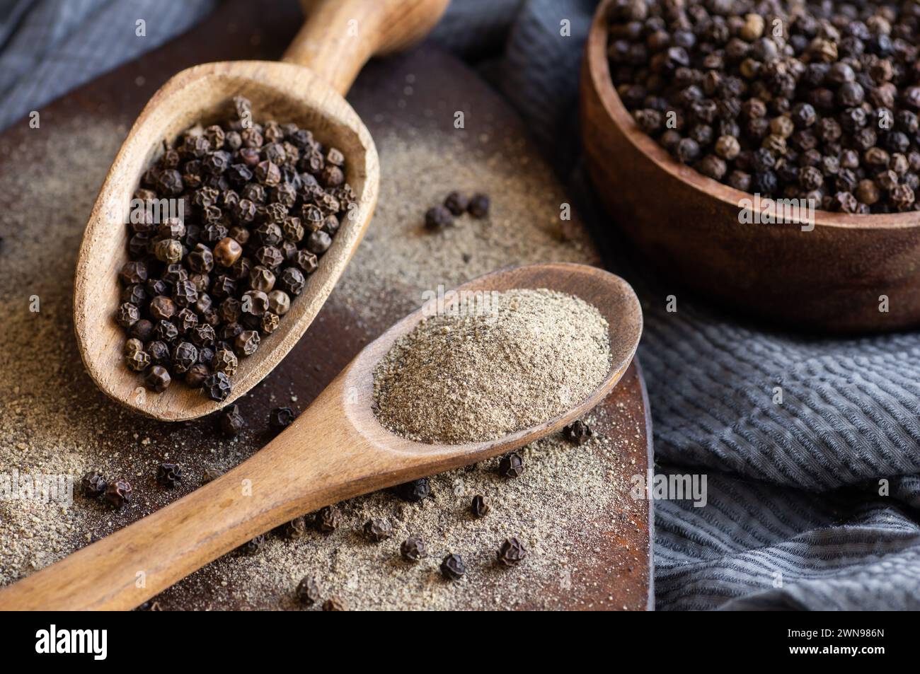 Un mucchio di pepe nero, grani di pepe in cucchiaio con polvere macinata su fondo rustico, concetto di pepe a base di spezie secche Foto Stock