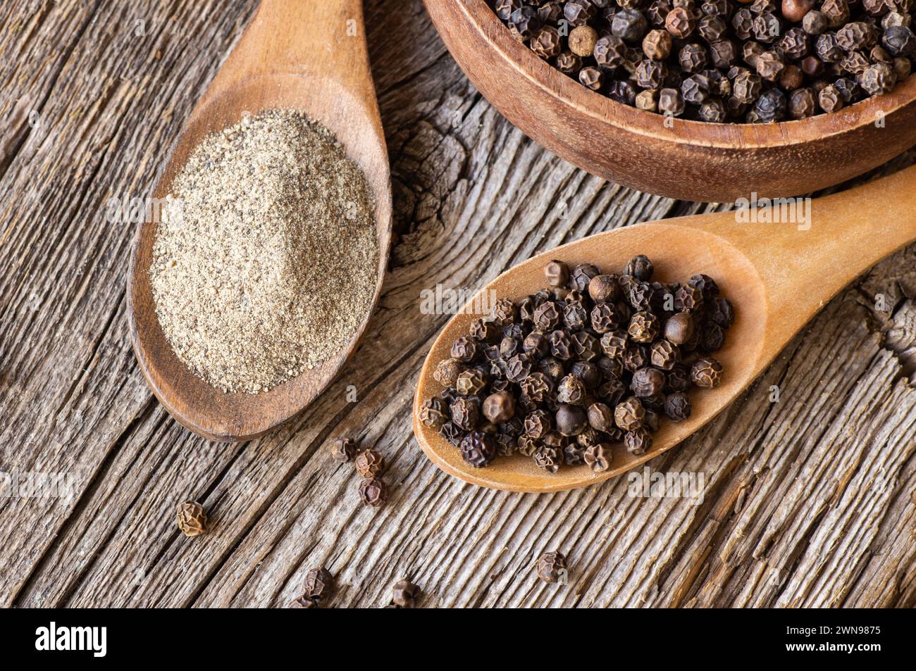Un mucchio di pepe nero, grani di pepe in cucchiaio con polvere macinata su fondo rustico, concetto di pepe a base di spezie secche Foto Stock