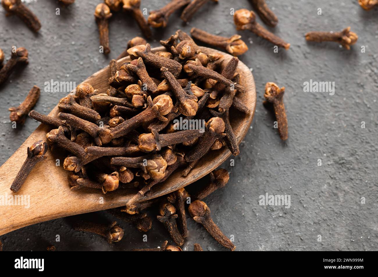Chiodi di garofano secchi in pala di legno o cucchiaio su tavola rustica, concetto di spezie fresche alle erbe Foto Stock