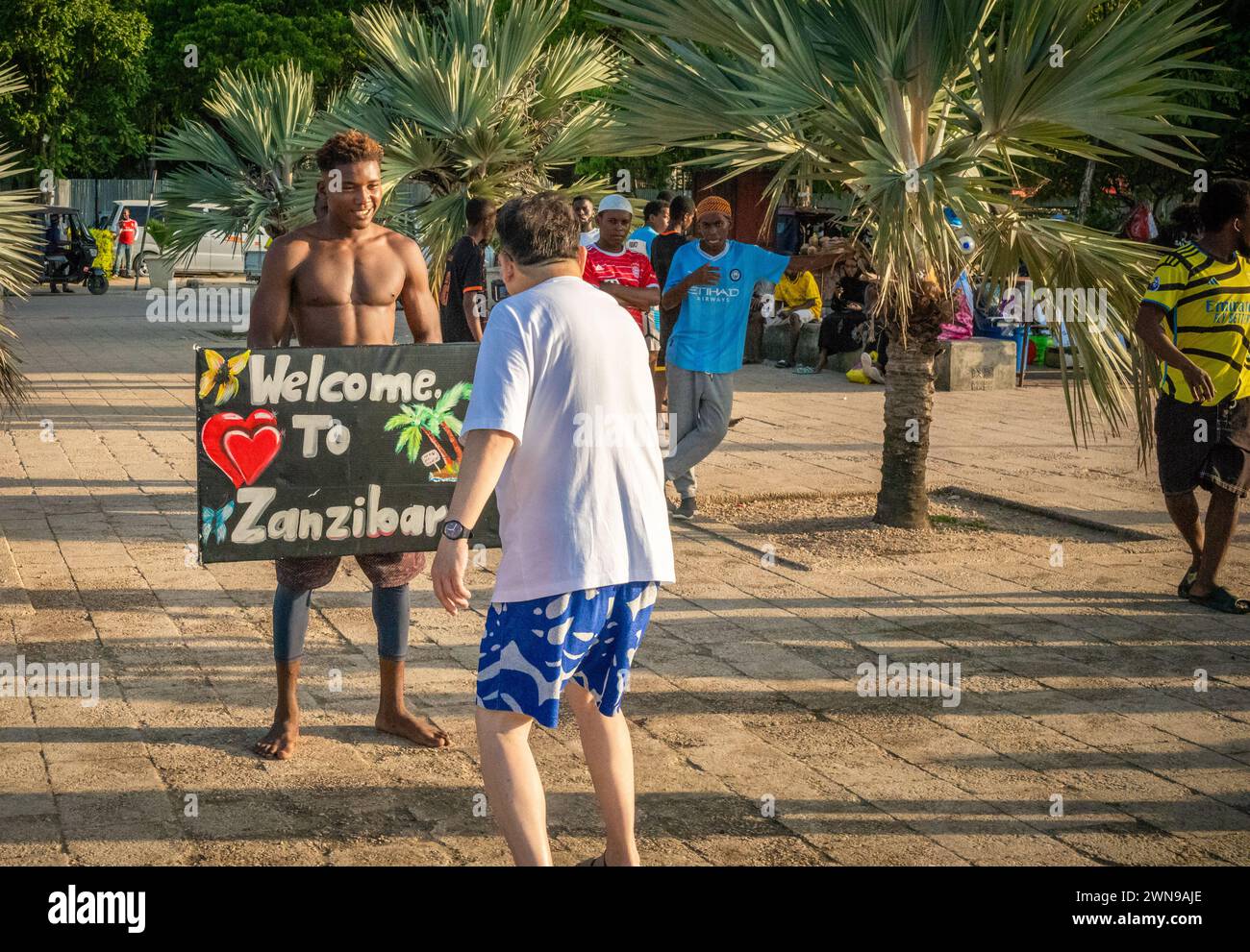 Un turista cinese filma un giovane sul lungomare di Stone Town, Zanzibar, Tanzania Foto Stock