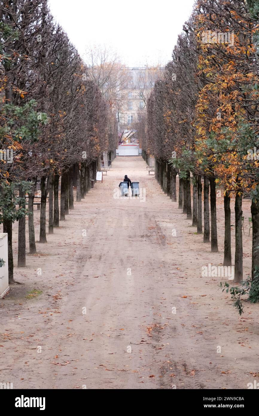 Una persona che trasporta due bidoni della spazzatura lungo un sentiero sabbioso fiancheggiato da alberi. Parigi Foto Stock