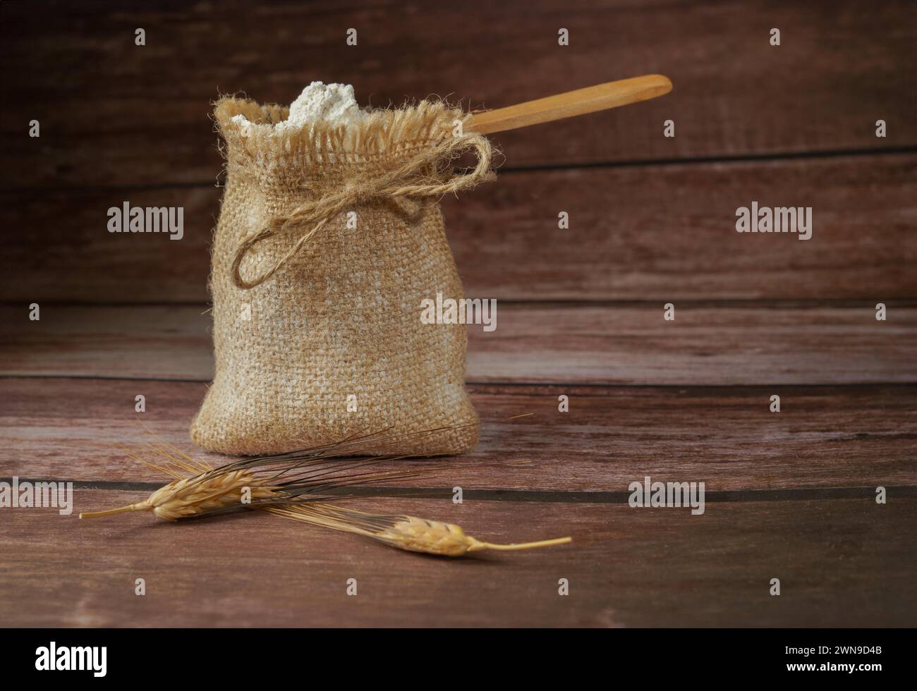 Sacco di scaglie con farina in un cucchiaio di legno su un tavolo di legno e orecchie di grano, sfondo con ombre e spazio per copiare Foto Stock