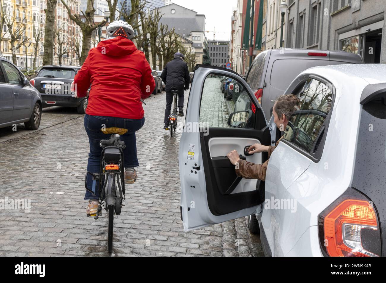 Un autista apre la porta della sua auto con il "Dutch Reach", mentre passa un ciclista, a Bruxelles, venerdì 1 marzo 2024. Il Parlamento europeo ha approvato una nuova norma per migliorare la sicurezza dei ciclisti. In futuro, ai conducenti verrà insegnato ad aprire la porta della vettura nel modo corretto. Il cosiddetto REACH olandese, che fa girare il conducente e guarda sullo specchietto retrovisore e sulle spalle, deve diventare lo standard in Europa per evitare incidenti con le porte aperte. BELGA FOTO NICOLAS MAETERLINCK BELGA FOTO NICOLAS MAETERLINCK Foto Stock