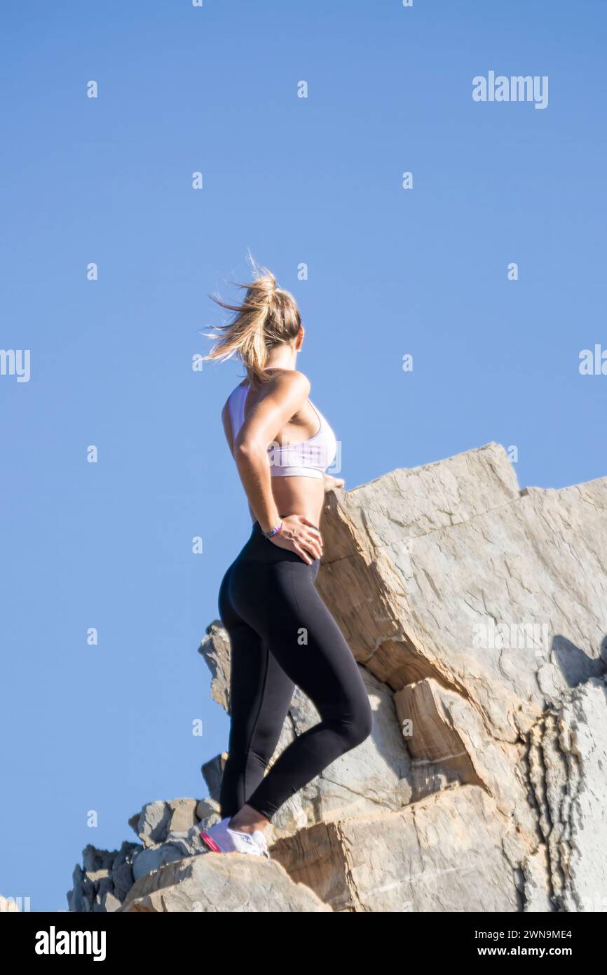 una donna con canotta rosa e leggings neri è in piedi su una roccia. Sta guardando il cielo Foto Stock una donna con canotta rosa e leggings neri è in piedi su una roccia. Sta guardando il cielo Foto Stock