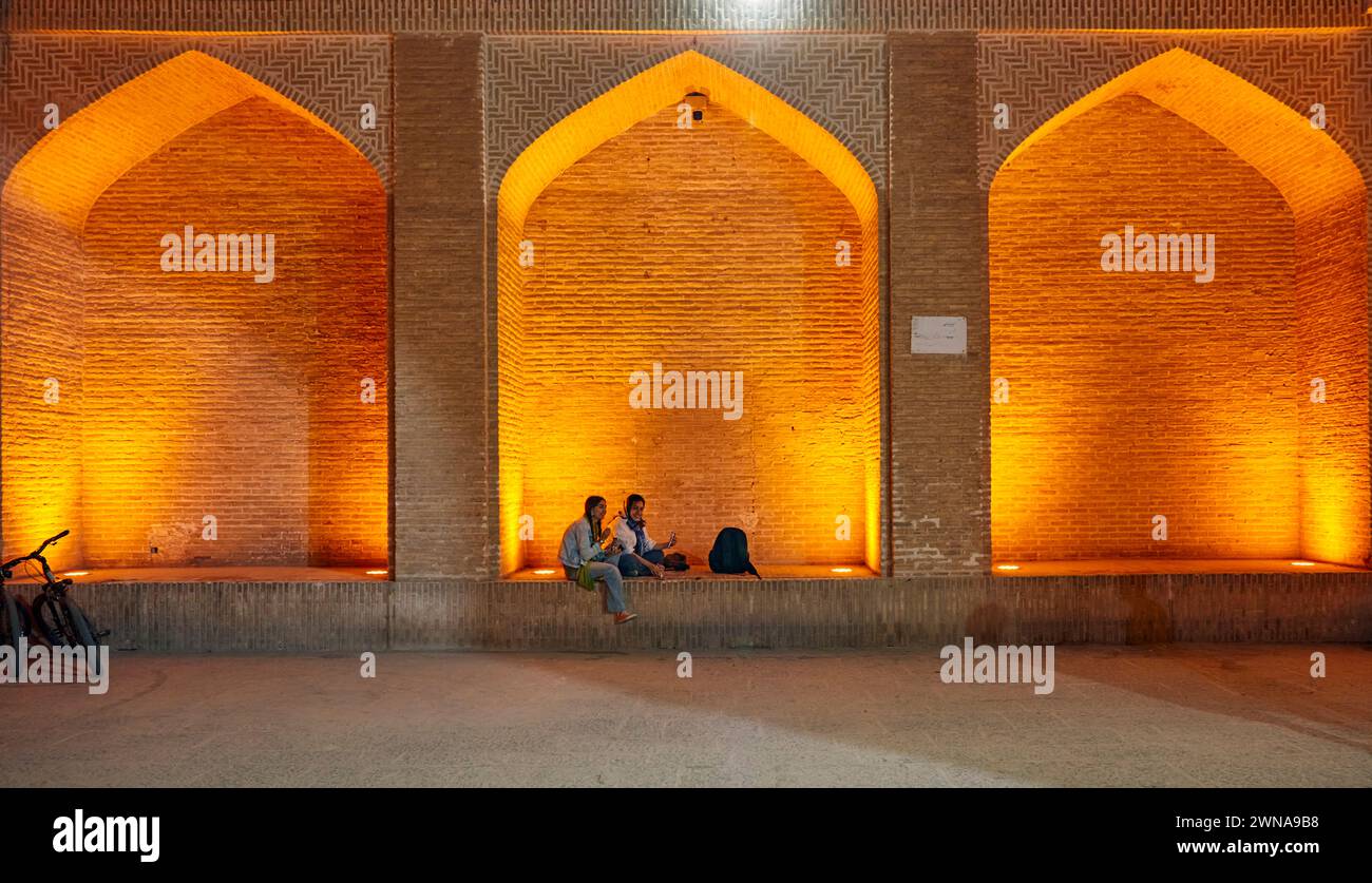 Due giovani ragazze iraniane si siedono insieme in un'alcova illuminata di notte. Città vecchia di Yazd, Iran. Foto Stock