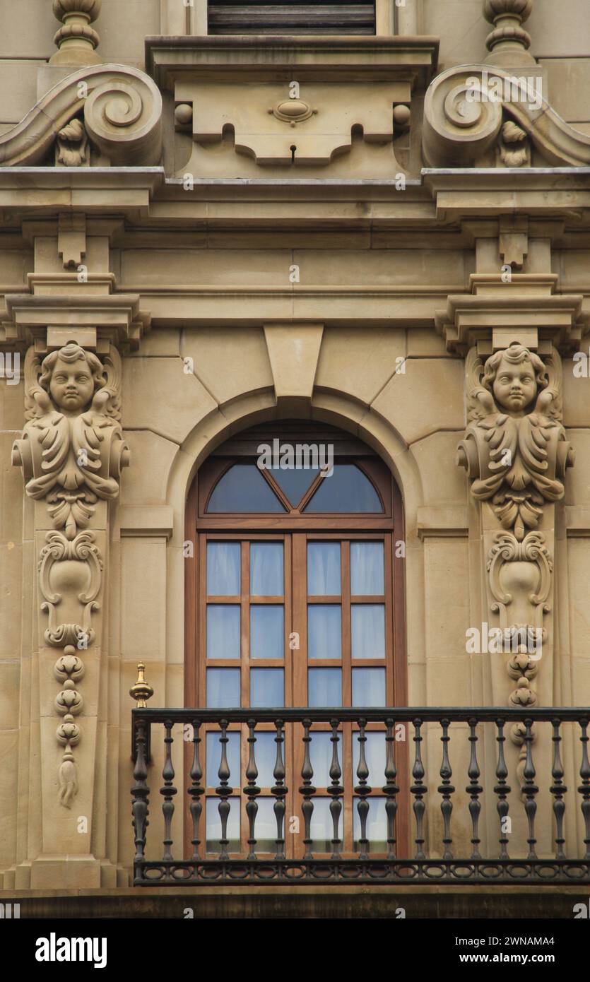 Balcone in pietra adornato con facce intagliate e ringhiere in ferro su un edificio storico a San Sebastian, Spagna Foto Stock