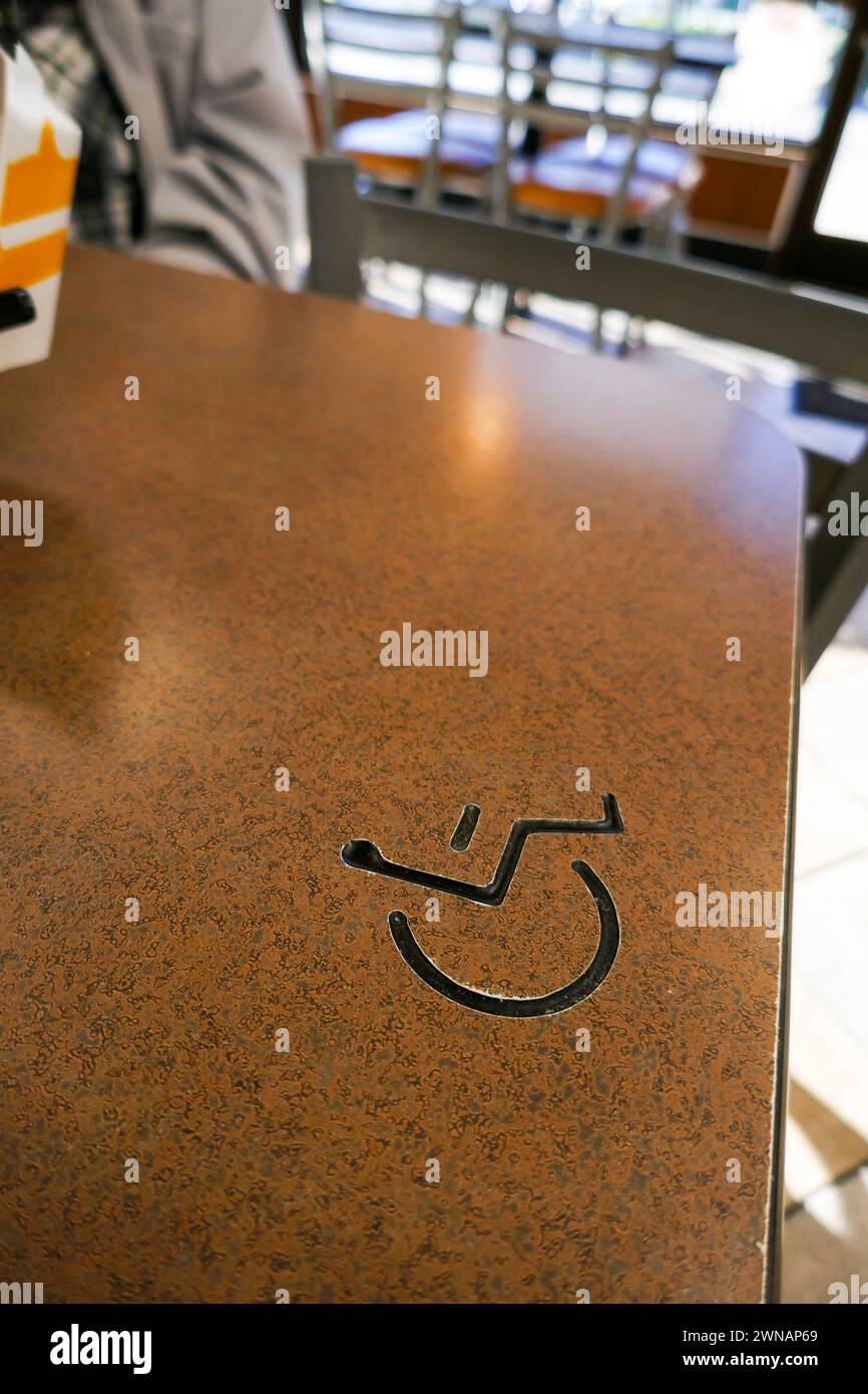 Tavolo in un fast food locale, con la designazione di posti a sedere per disabili, simbolo incorporato sulla superficie del tavolo. Foto Stock