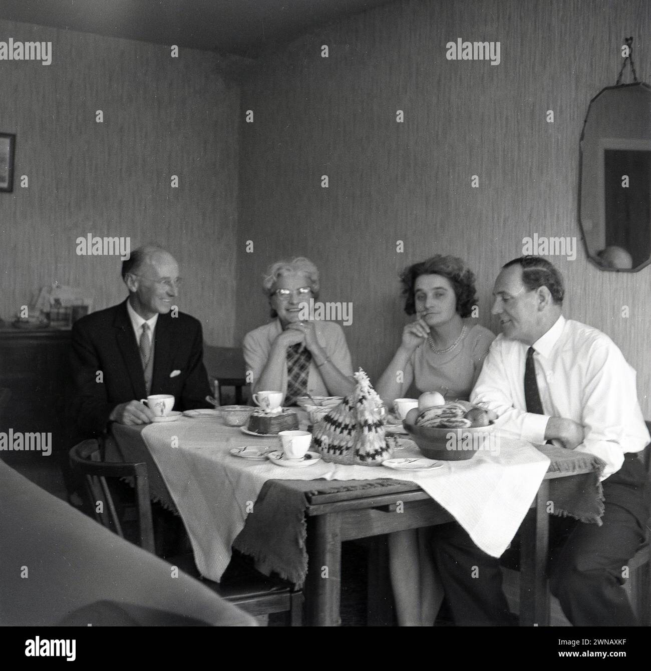 Anni '1950, due coppie di mezza età sedute su un tavolo coperto di stoffa in una sala da pranzo che si gusta una tazza di tè e una conversazione, Inghilterra, Regno Unito. Foto Stock