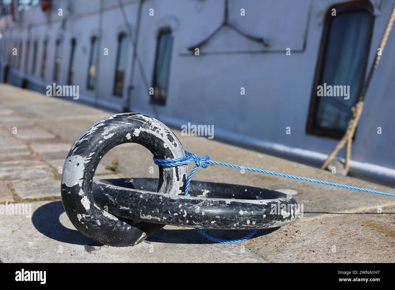 Sottile corda di nylon legata a un grande anello di ormeggio in ferro con nave e finestre sullo sfondo Foto Stock