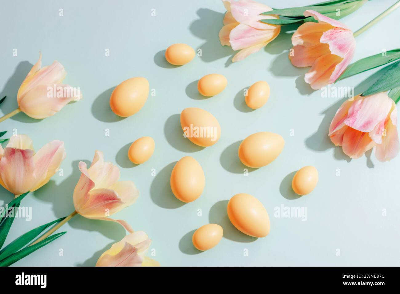 Uova di Pasqua gialle e fiori di tulipani su sfondo verde alla luce del sole. Concetto di Pasqua. Vista dall'alto, disposizione piatta. Foto Stock