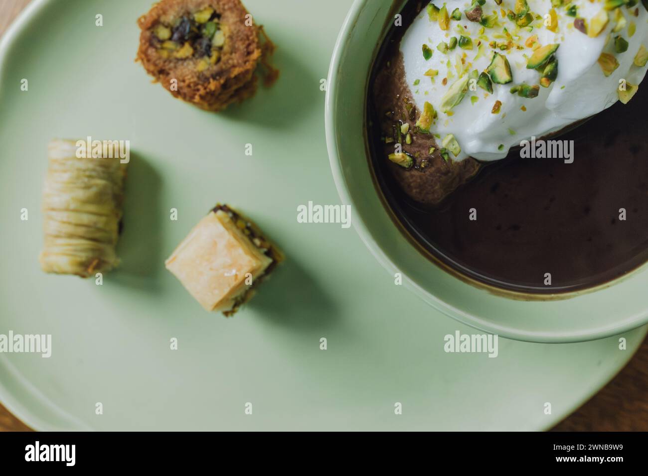 Primo piano di cioccolato bevuto in una tazza verde abbinata e piatto con panna e pistacchi e dessert baklava assortiti Foto Stock