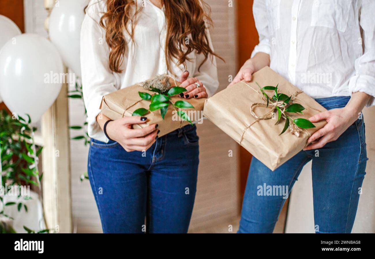 Regali avvolti in carta kraft nelle mani degli ospiti alla festa Baby Shower regali decorati con foglie fresche Foto Stock