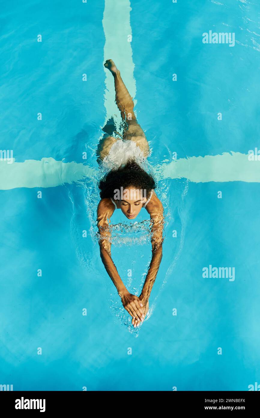 vista dall'alto della giovane donna nera che nuota in acque cristalline e blu della piscina, serena e tranquilla Foto Stock