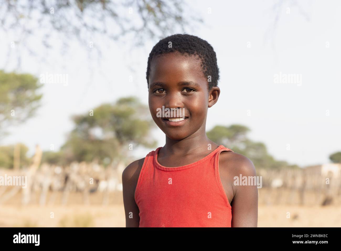 ragazza africana con un grande sorriso di toothy , nel villaggio, in piedi nel cortile accanto ad un albero Foto Stock