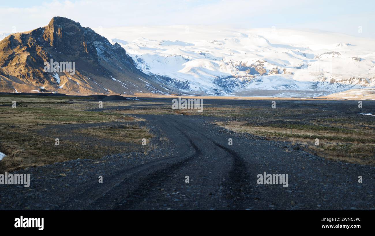 Strada in Islanda meridionale in inverno con montagne coperte di neve a Myrdalsjökull e cielo blu sullo sfondo Foto Stock