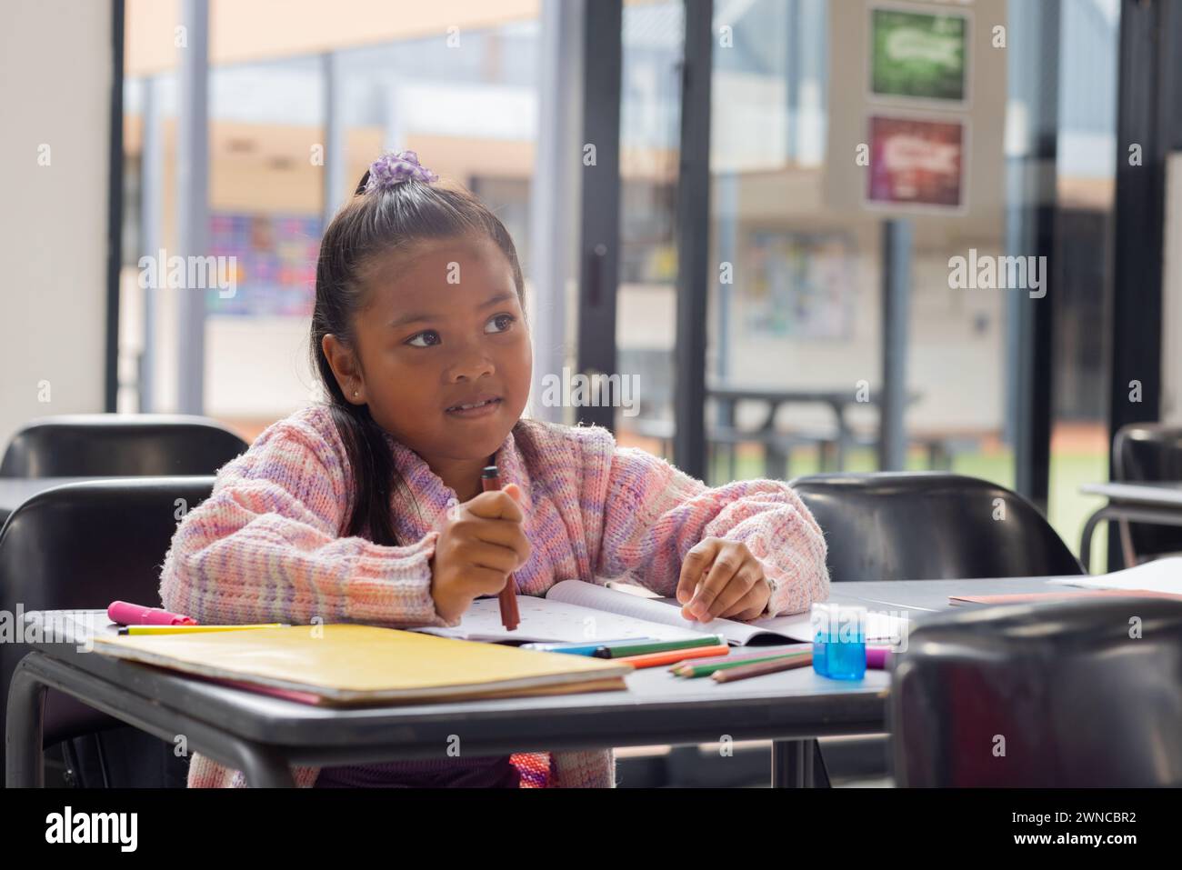 Una ragazza birazziale con un'espressione concentrata scrive su un taccuino a scuola Foto Stock