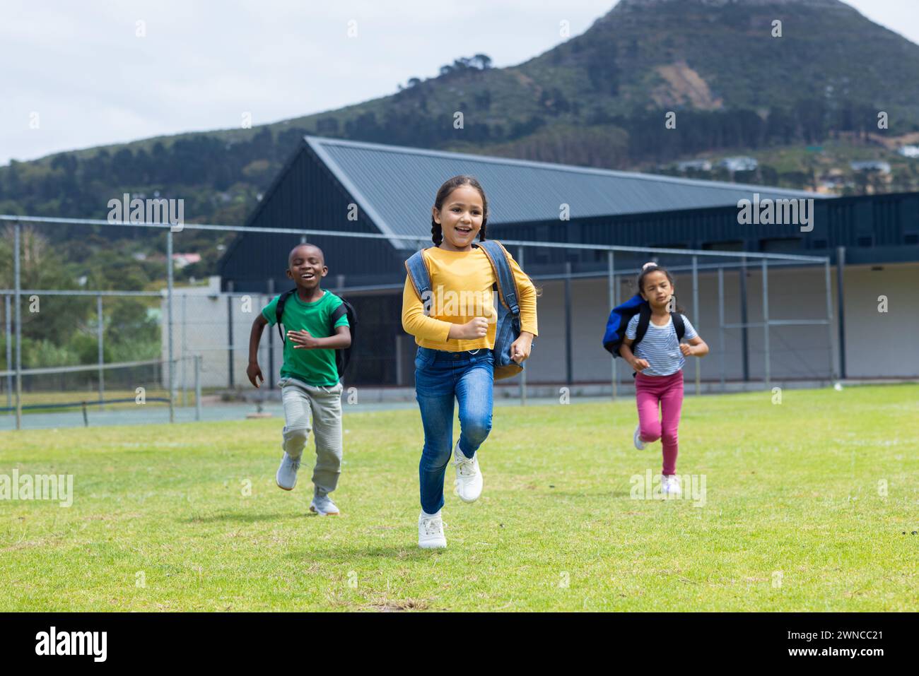 Tre bambini corrono gioiosamente in un campo erboso durante il giorno a scuola Foto Stock