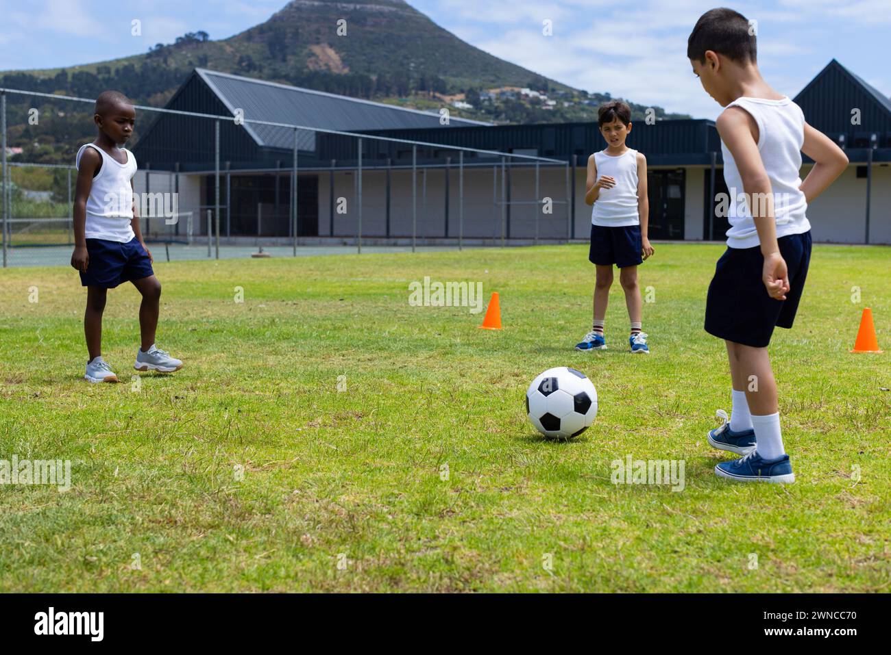 Tre ragazzi sono in piedi su un campo erboso con un pallone da calcio, pronti a giocare a scuola Foto Stock