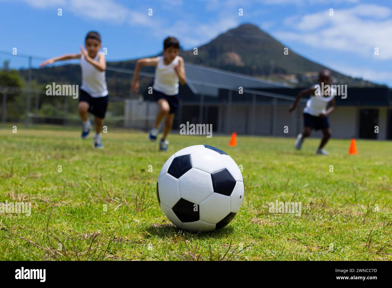 Un pallone da calcio a fuoco con tre bambini che corrono dietro a scuola Foto Stock