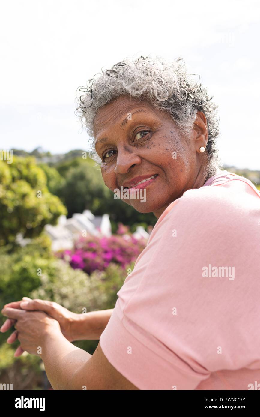 Donna birazziale anziana con capelli grigi ricci sorride dolcemente all'aperto Foto Stock