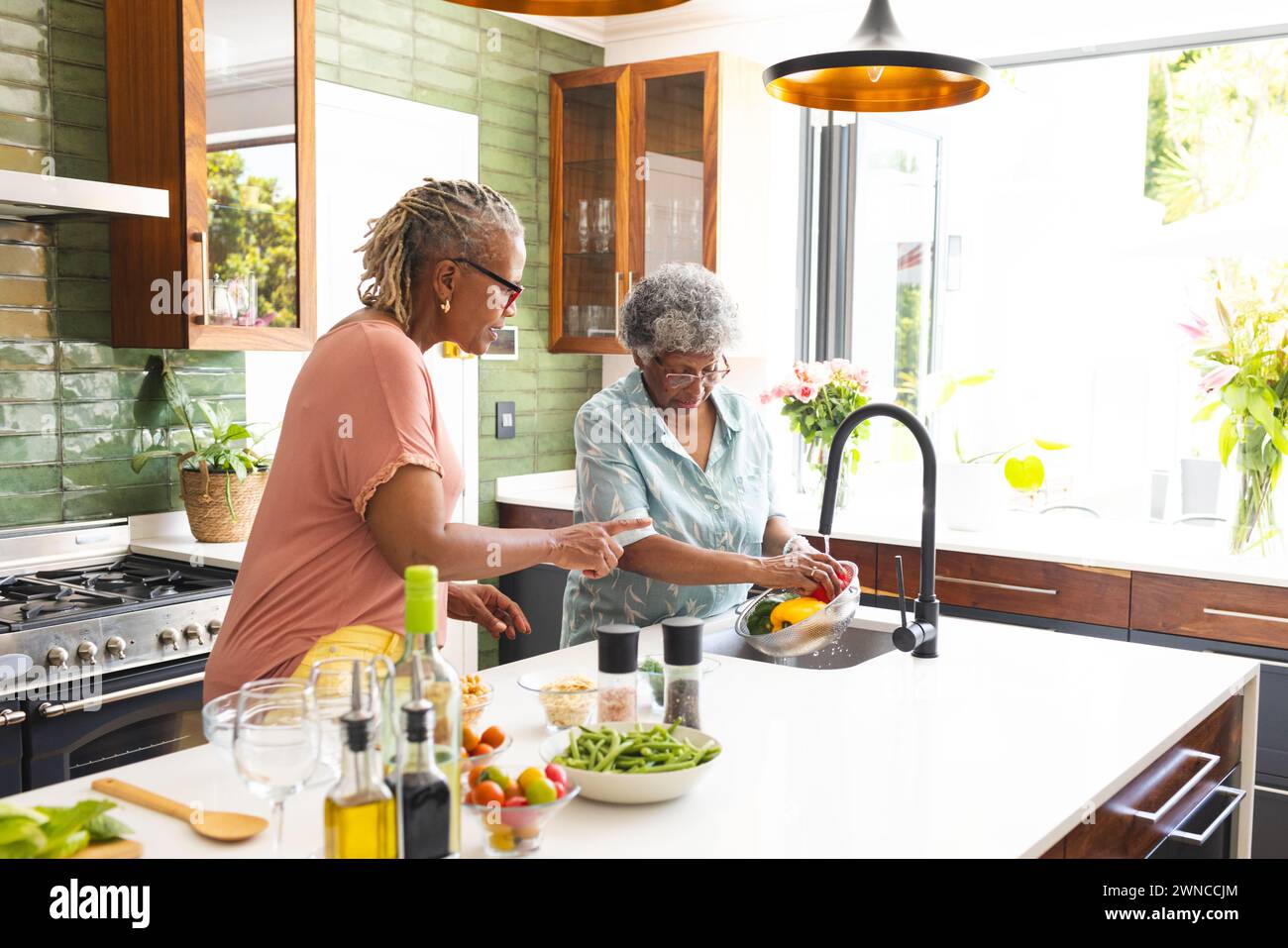 La donna afroamericana anziana e la donna birazziale anziana stanno lavando le verdure in una cucina Foto Stock