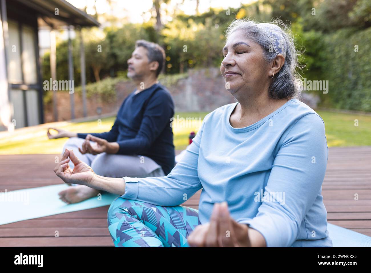 Donna e uomo birazziali senior meditano in un tranquillo giardino a casa Foto Stock