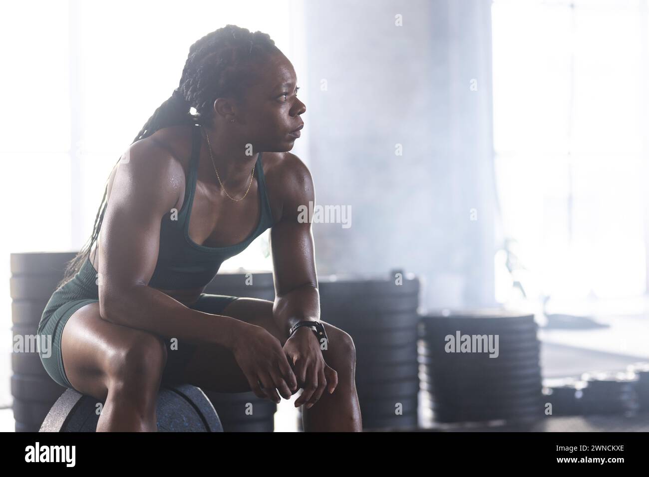 L'atleta birazziale in abbigliamento da palestra riposa con determinazione, incarnando la forza. Foto Stock