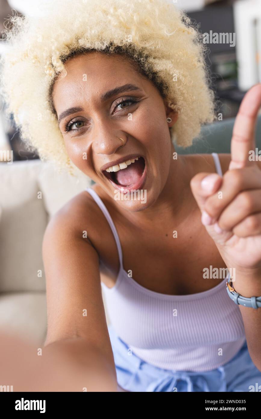 La giovane donna birazziale con capelli biondi ricci sorride e punta verso l'alto durante le videochiamate Foto Stock