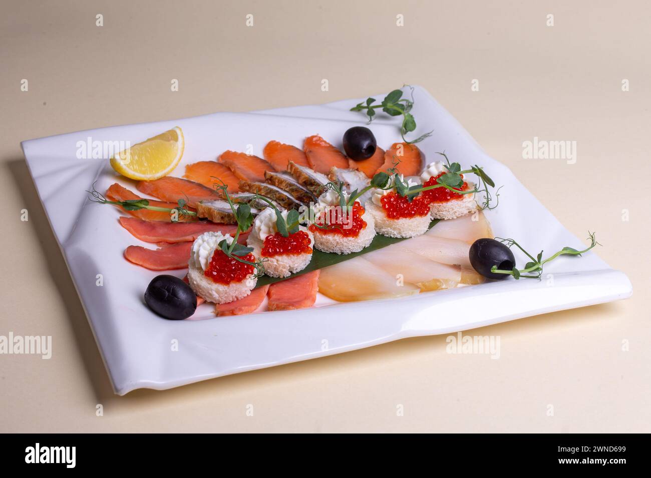 Un piatto di pesce fresco preparato ad arte - salmone, trota, caviale e gamberi - su un piatto bianco con fette di limone e verdure. Un'attrattiva visiva Foto Stock