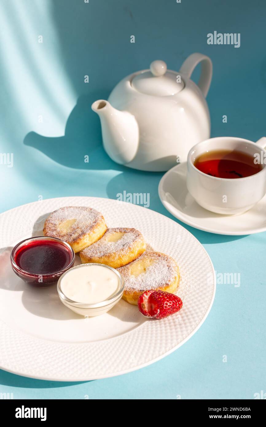 Gusta una sana colazione con soffici pancake al formaggio conditi con marmellata, fragole fresche e un cucchiaio di panna acida. Dai energia alla tua giornata Foto Stock