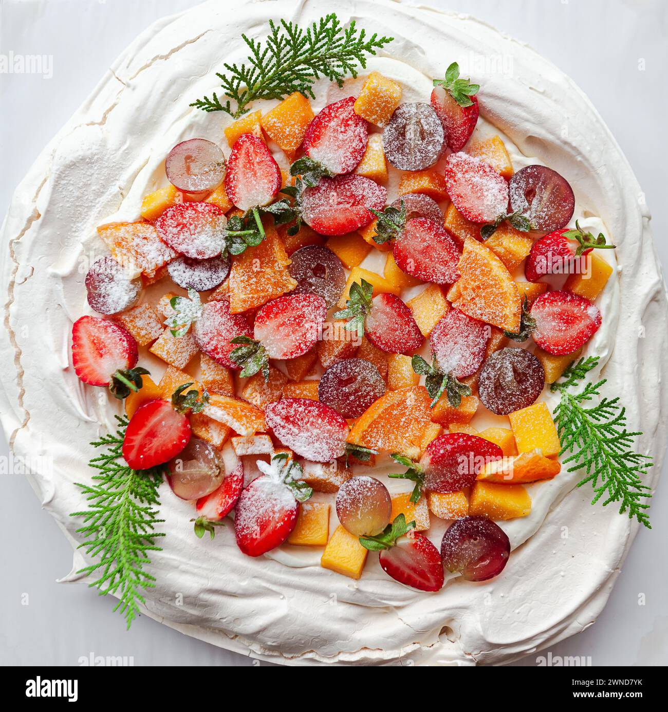 Una torta pavlova bianca adornata con frutti di bosco freschi e un tocco di verde Foto Stock