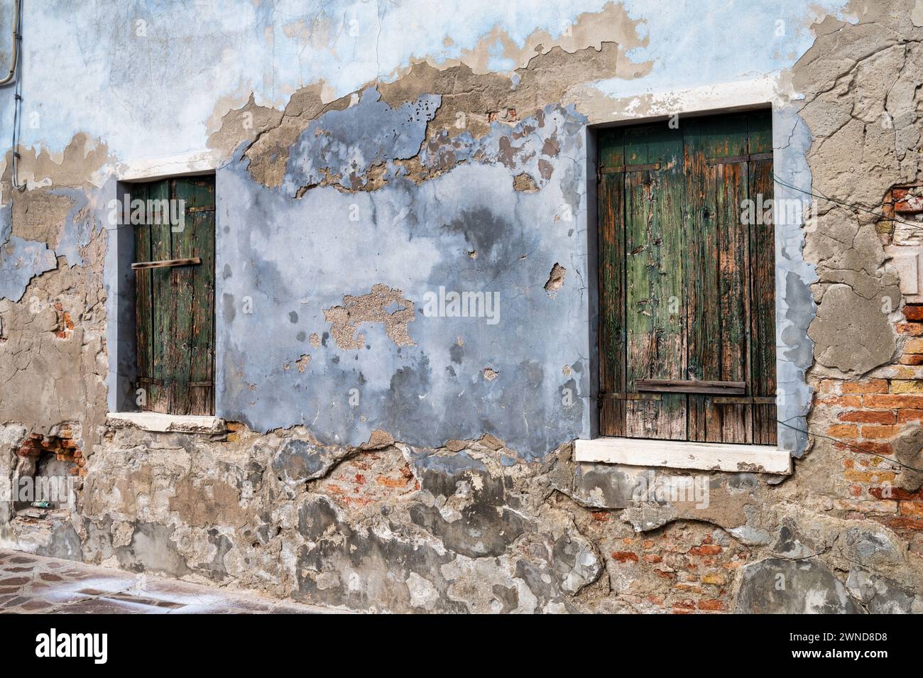 Mattoni esposti su un vecchio muro in gesso a Burano in Italia con due serrature in legno. Foto Stock