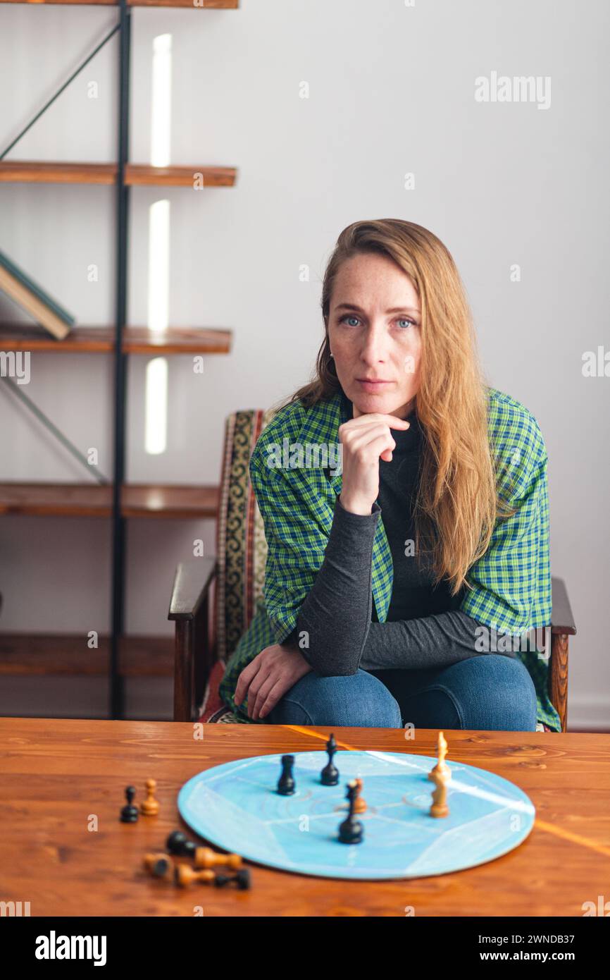 Composizione verticale. Una donna decisa siede accanto al tavolino da caffè e guarda con attenzione i pezzi degli scacchi su un cerchio blu. Psicologia. Fase-B. Foto Stock