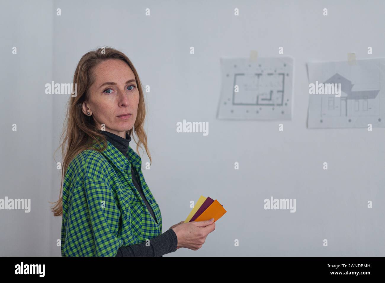 Donna adulta che sceglie il colore per la piccola casa il cui progetto è attaccato al muro. Foto Stock